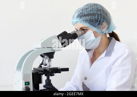 Female scientist looking through microscope in modern chemical laboratory doing some research. Analyzing samples using a microscope Stock Photo