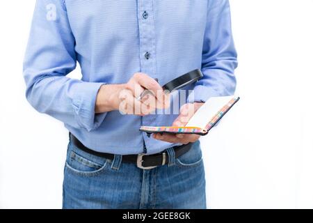 Man in blue shirt and blue pants examining a paper notebook with a magnifying glass. Photo on white background. Copy space. Stock Photo