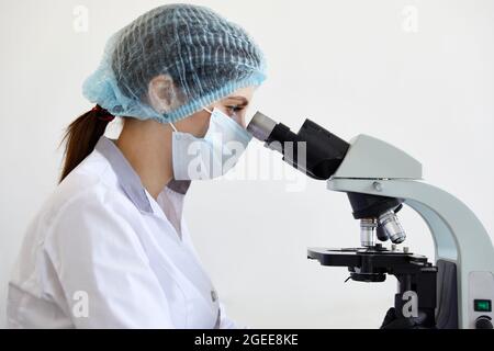 Female scientist looking through microscope in modern chemical laboratory doing some research. Analyzing samples using a microscope Stock Photo