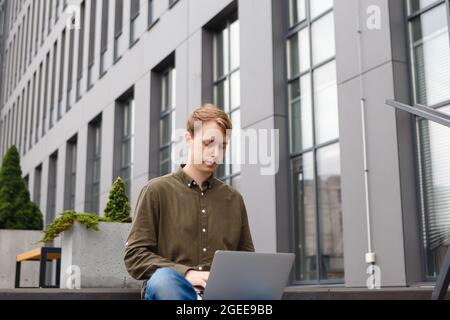 man working on laptop sitting on the stairs of business center Stock Photo