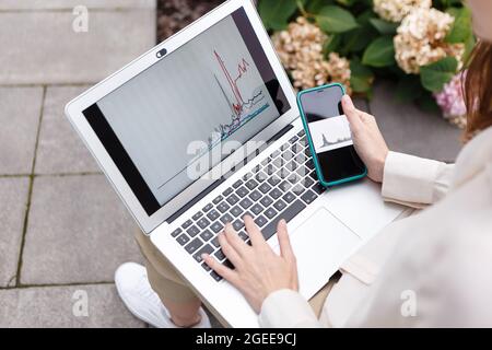 woman holding laptop and smartphone watching bitcoin growth chart Stock Photo