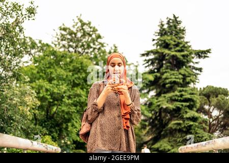 Stock photo of beautiful muslim woman walking and looking her cellphone. She is wearing a hiyab Stock Photo