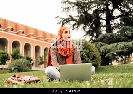 Stock Photo of Muslim woman using computer siting on the grass. she is wearing a hiyab