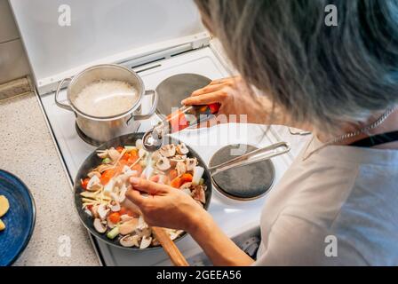 Woman cooks dinner in Asian style, adds oyster sauce to a frying pan Stock Photo