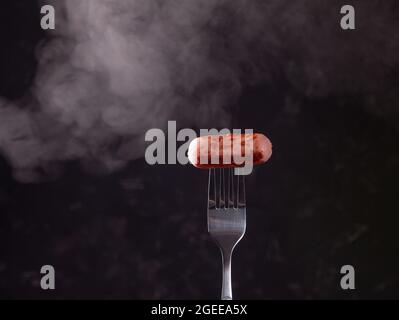 Grilled sausage on a fork fuming smoke dark black background Stock Photo