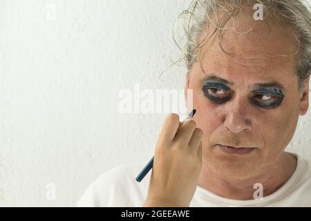 hand of a girl painting the eyes of a serious mature man with cosmetic on white background Stock Photo