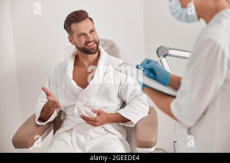 Smiling man talks to administrator filling form while examining patient in clinic Stock Photo