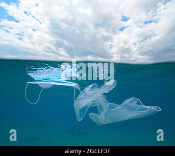 Plastic pollution underwater, protective face mask and gloves under sea with cloudy sky, split view over under water surface, COVID-19 pandemic Stock Photo