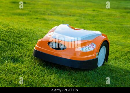 Automatic lawn robot mower moves on the grass slope, lawn. Close up side view Stock Photo