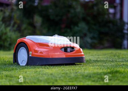 Automatic lawn robot mower moves on the short cut grass, lawn. Close up side view with blurry background Stock Photo