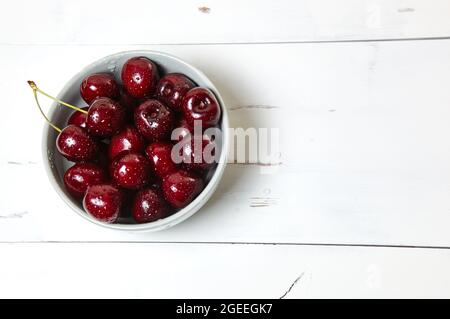 Sweet cherries in a ceramic bowl on wooden background, closeup. Fresh ripe sweet cherries in a bowl with droplets of water, top view Stock Photo