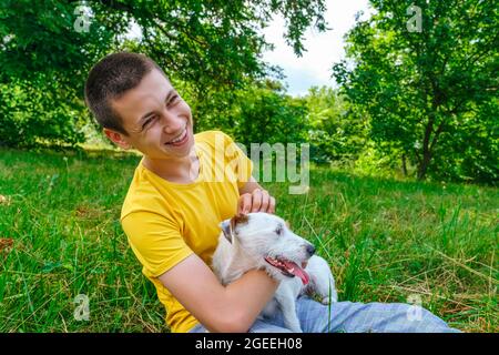 Man sits on the grass and strokes dog Jack Russell terrier in summer park  Stock Photo