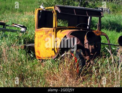Old truck sits in the tall grass, rusting, wrecked, faded and retired.  Truck sits on a backroad in Alaska. Stock Photo