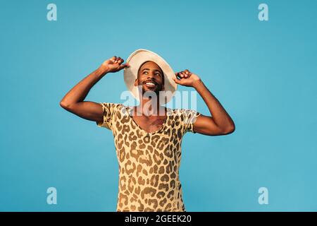 Smiling stylish man holding his straw hat and looking up against the blue background Stock Photo