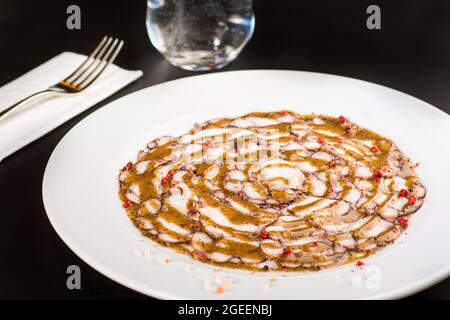 Octopus Carpaccio. Seafood raw octopus slices with olive oil and black pepper on a white plate. Stock Photo