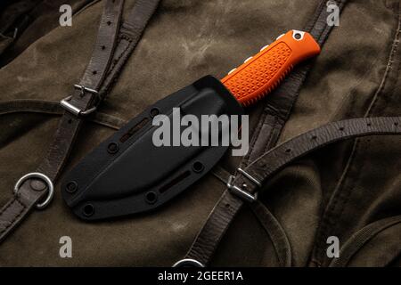 A hunting knife with a orange rubberized grip on a khaki canvas backpack. Weapons for self-defense and survival. Stock Photo