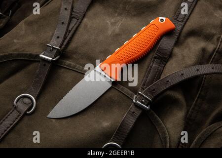 A hunting knife with a orange rubberized grip on a khaki canvas backpack. Weapons for self-defense and survival. Stock Photo