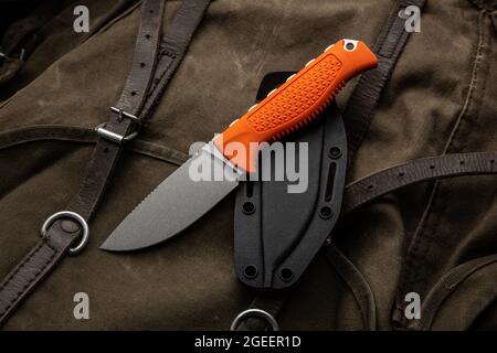 A hunting knife with a orange rubberized grip on a khaki canvas backpack. Weapons for self-defense and survival. Stock Photo