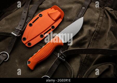 A hunting knife with a orange rubberized grip on a khaki canvas backpack. Weapons for self-defense and survival. Stock Photo