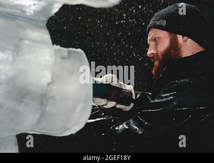 Professional ice carver sculpting block of ice with electric dremel Stock Photo