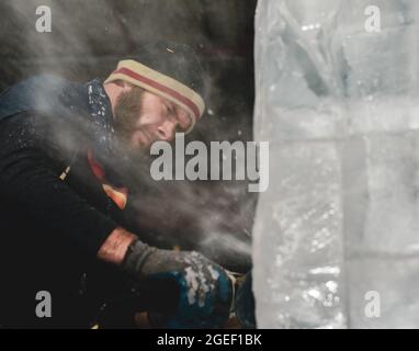 Professional ice carver sculpting block of ice with electric dremel Stock Photo