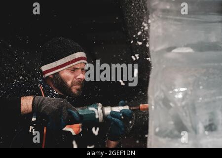 Professional ice carver sculpting block of ice with electric dremel Stock Photo