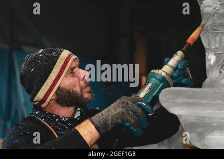 Professional ice carver sculpting block of ice with electric dremel Stock Photo