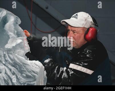 Professional ice carver sculpting block of ice with electric dremel Stock Photo