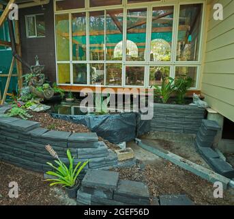 Garden feature under construction with curved brick retaining walls surrounding raised garden beds and fish pond in a fernery, in Australia Stock Photo