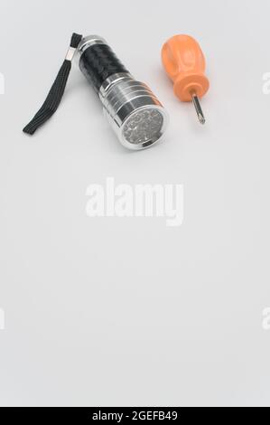 Vertical shot of a screwdriver with an orange handle and a small flashlight on a white background Stock Photo