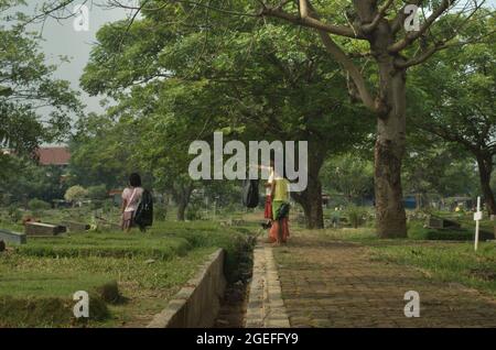 Children working by collecting plastic waste at Pondok Kelapa public cemetery in East Jakarta, Indonesia. Some of them work on daily basis; mostly by offering service of grave cleaning. Stock Photo