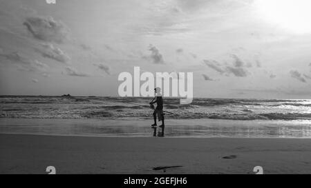 Grayscale shot of a person's silhouette walking down the seashore Stock Photo