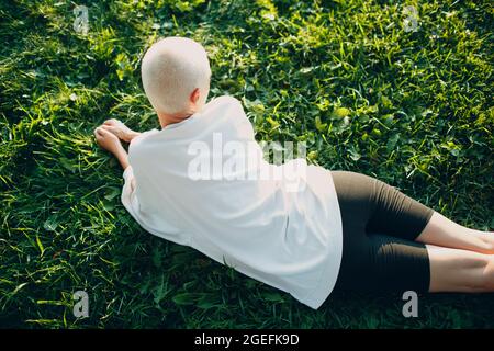 Portrait of young smiling millenial european short haired woman laying on stomach green grass meadow summer park overhead top aerial view. Beautiful happy blonde girl outdoor. Stock Photo