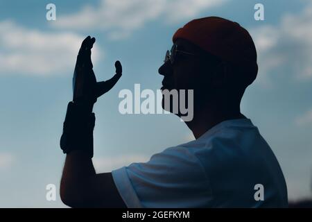 Young disabled man with artificial prosthetic hand silhouette against sky Stock Photo