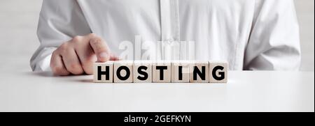 Businessman pressing his finger on the wooden cubes with the word HOSTING. Hosting service provider concept. Stock Photo