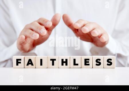 Man holding his hands over the wooden cubes with the word faithless. Disbelief or unfaithful concept. Stock Photo