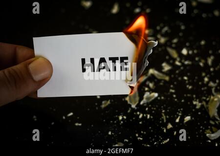 burning hate, human hand holding the word hate written on a paper burning with flame and ashes on a black background, concept Stock Photo