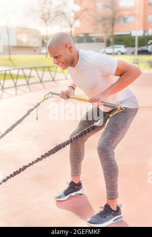 Atlhetic latin sportsman exercising with a fitness strap in the park Stock Photo
