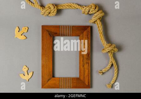 Empty photo frame and rope against a gray background. Wooden picture frame. Natural rope. Wooden anchors. Top view. Stock Photo