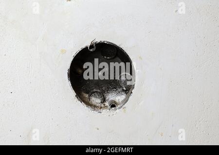 Black mounting box for electrical outlets in a light gray plastered wall. Scratched old wall in close-up. Abstract background. Architecture Stock Photo