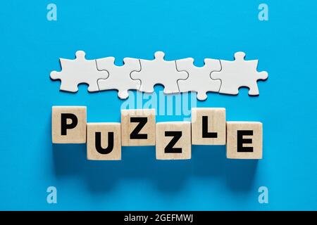 The word puzzle on wooden cubes with a connected line of jigsaw puzzle. Jigsaw puzzle game or mystery concept. Stock Photo