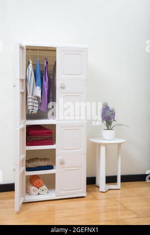 Opened plastic wardrobe with clothing in bedroom background Stock Photo