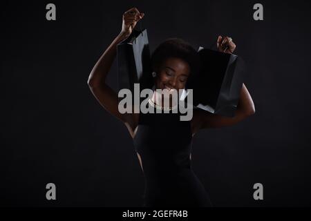 African american happy woman with afro hairstyle holds black shopping bags. Black Friday concept. Stock Photo