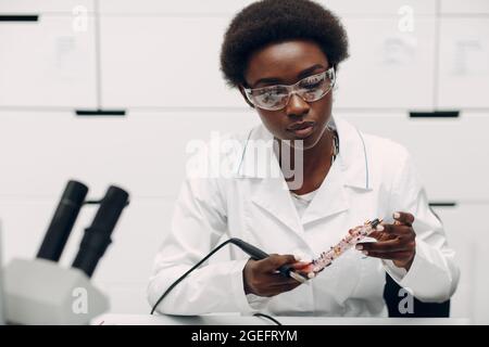 Scientist african american woman working in laboratory with soldering ironand checking electronic plate board. Research and development of electronic devices by color black woman. Stock Photo