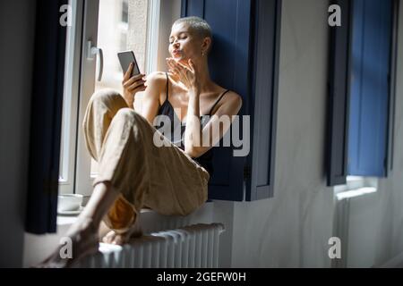Stylish woman talking on phone at window Stock Photo