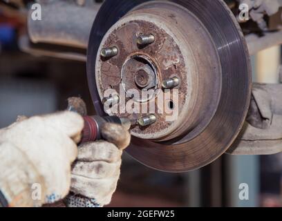 The man's hands are turning the worn out rear brake disc with a screwdriver. In the garage, a person changes the failed parts on the vehicle. Small business concept, car repair and maintenance service Stock Photo