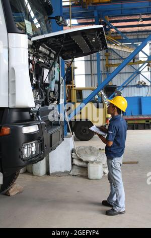 A mechanic is inspecting the engine of a truck and taking notes. Stock Photo