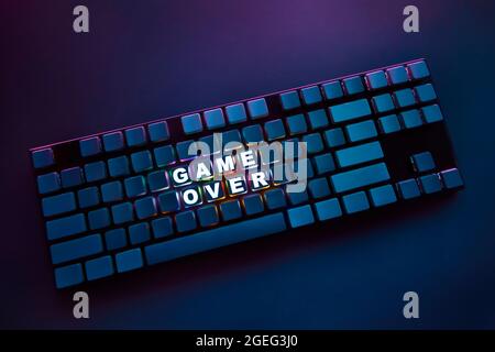 High angle view of computer keyboard with thin frame and backlighted inscription game over. Professional computer game playing, esport business and on Stock Photo