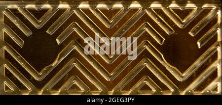 Thin, shiny, metallic-look sheet of plastic packaging. Gold coloured plastic with imprinted zig-zag pattern, Rubbish, trash. Background, abstract. Stock Photo