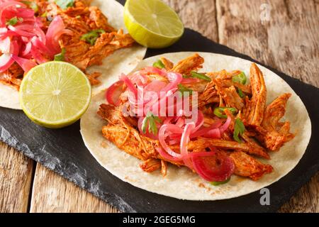 Cochinita pibil is a Mexican dish served with tortilla and marinated onion closeup in the slate board on the table. Horizontal Stock Photo